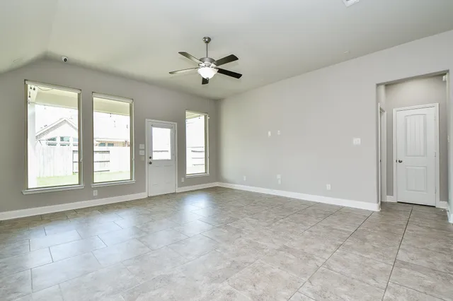 an empty room with chandelier fan and windows