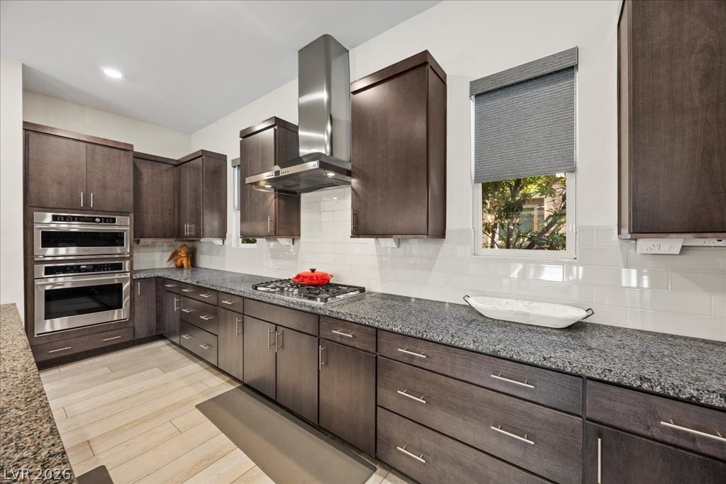 4262 Swift Street Las Vegas, NV 89135 - Photo 18 of 75 Kitchen featuring dark brown cabinetry, wall chimney exhaust hood, and dark stone countertops