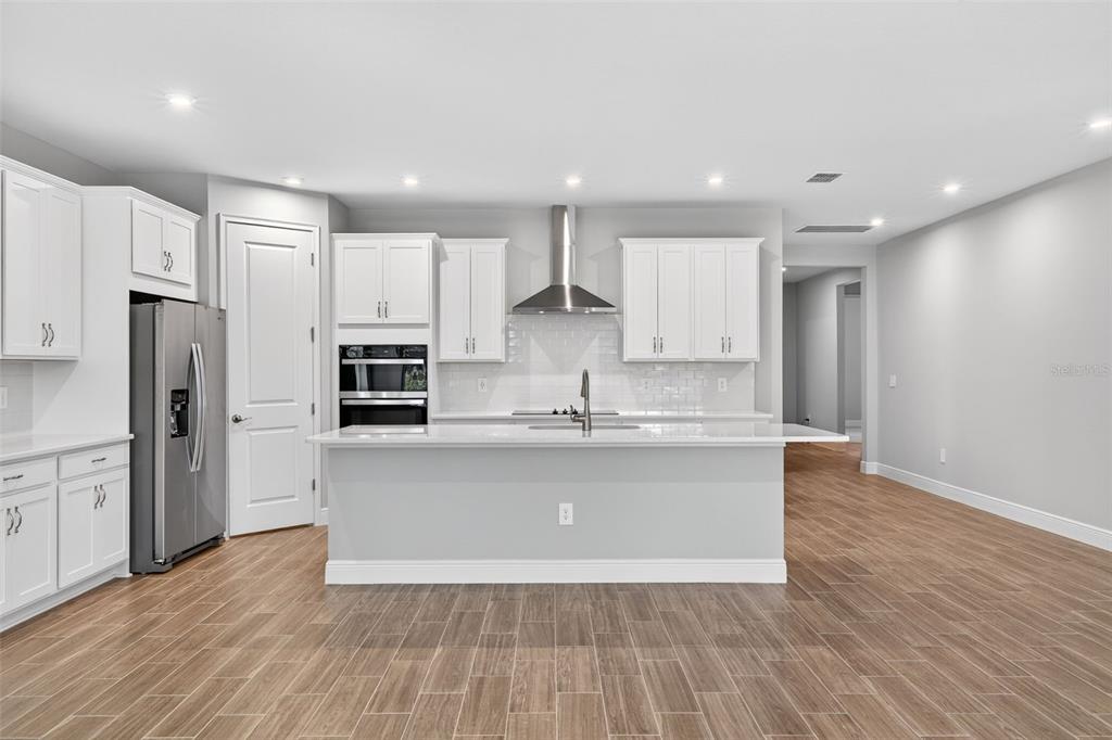 12349 49th Street East Parrish, FL 34219 - Photo 3 of 38 a large kitchen with stainless steel appliances granite countertop a large stove a refrigerator a sink and white cabinets with wooden floor