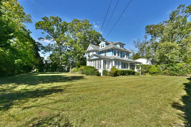 a view of a white house with a yard plants and large tree