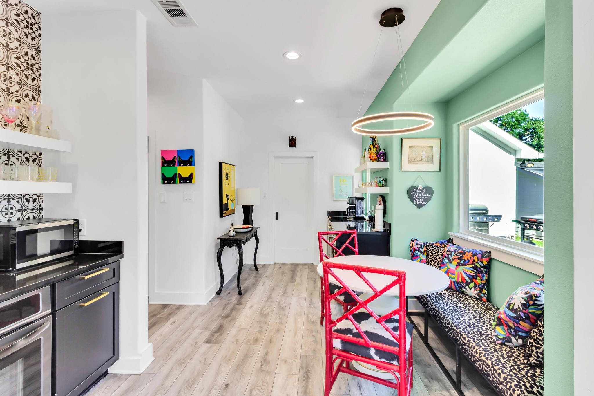 295 County Road 687 Angleton, TX 77515 - Photo 21 of 38 This bright kitchen nook features a large window for natural light, colorful seating with patterned cushions, and a modern circular pendant light. The adjacent kitchen area has sleek black cabinets, open shelves, and stylish patterned backsplash, creating a vibrant and welcoming space.