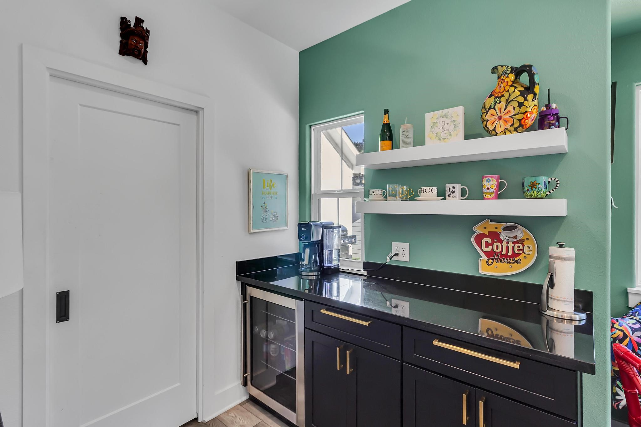 295 County Road 687 Angleton, TX 77515 - Photo 22 of 38 Cozy corner with a coffee bar setup, featuring a sleek black countertop, mini fridge, and open shelves displaying colorful mugs and decor. Bright and inviting with a small window adding natural light.