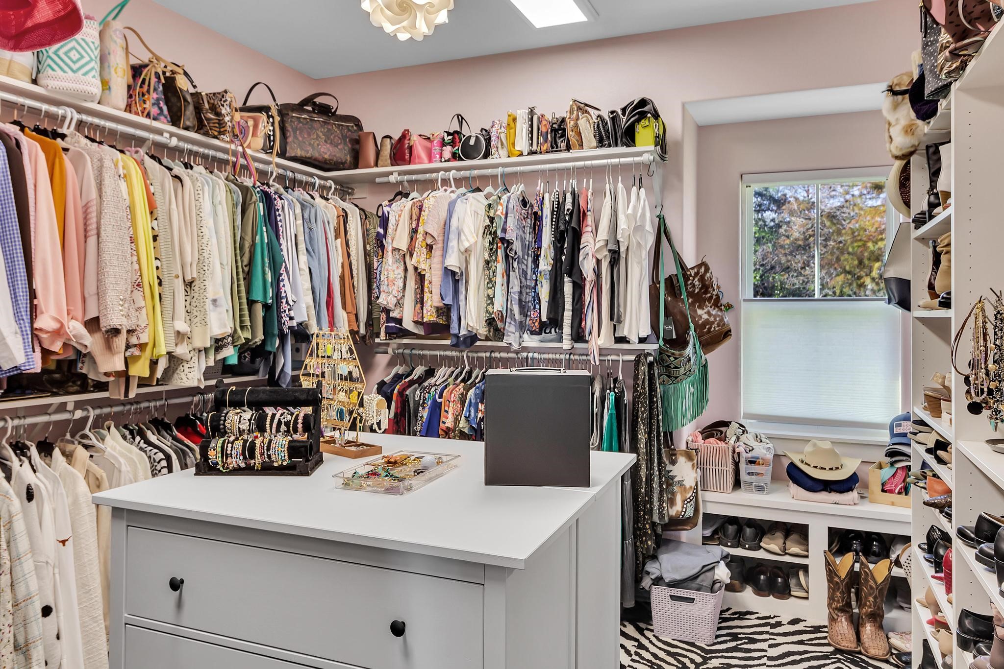 295 County Road 687 Angleton, TX 77515 - Photo 32 of 38 This spacious walk-in closet features ample hanging space, shelving, and a central island with drawers, ideal for organizing clothing and accessories. A large window provides natural light, enhancing the room's functionality and appeal.
