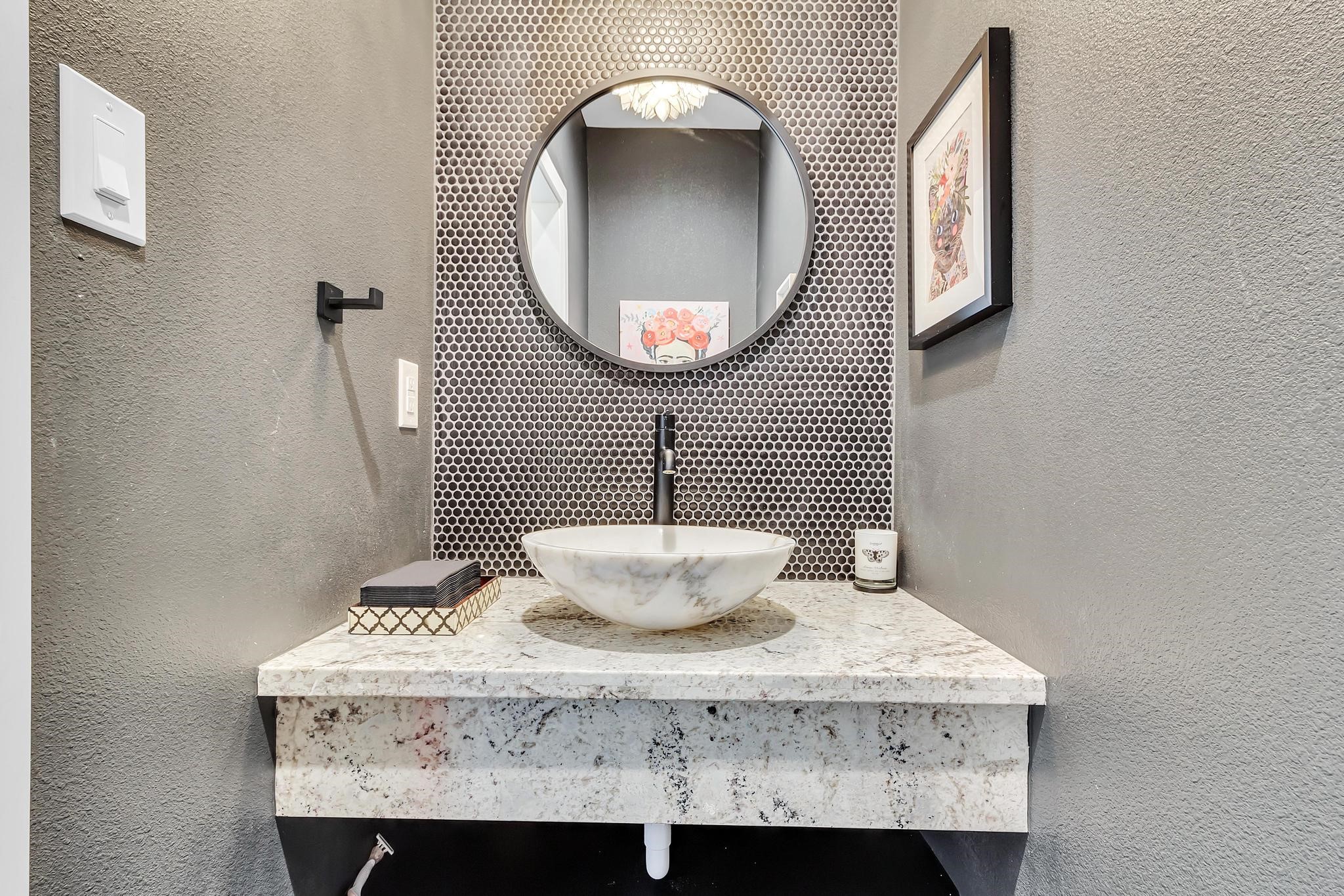 295 County Road 687 Angleton, TX 77515 - Photo 33 of 38 This bathroom features a stylish vanity with a marble vessel sink, a circular mirror, and a textured tile backsplash. Modern fixtures and gray walls add a sleek touch.