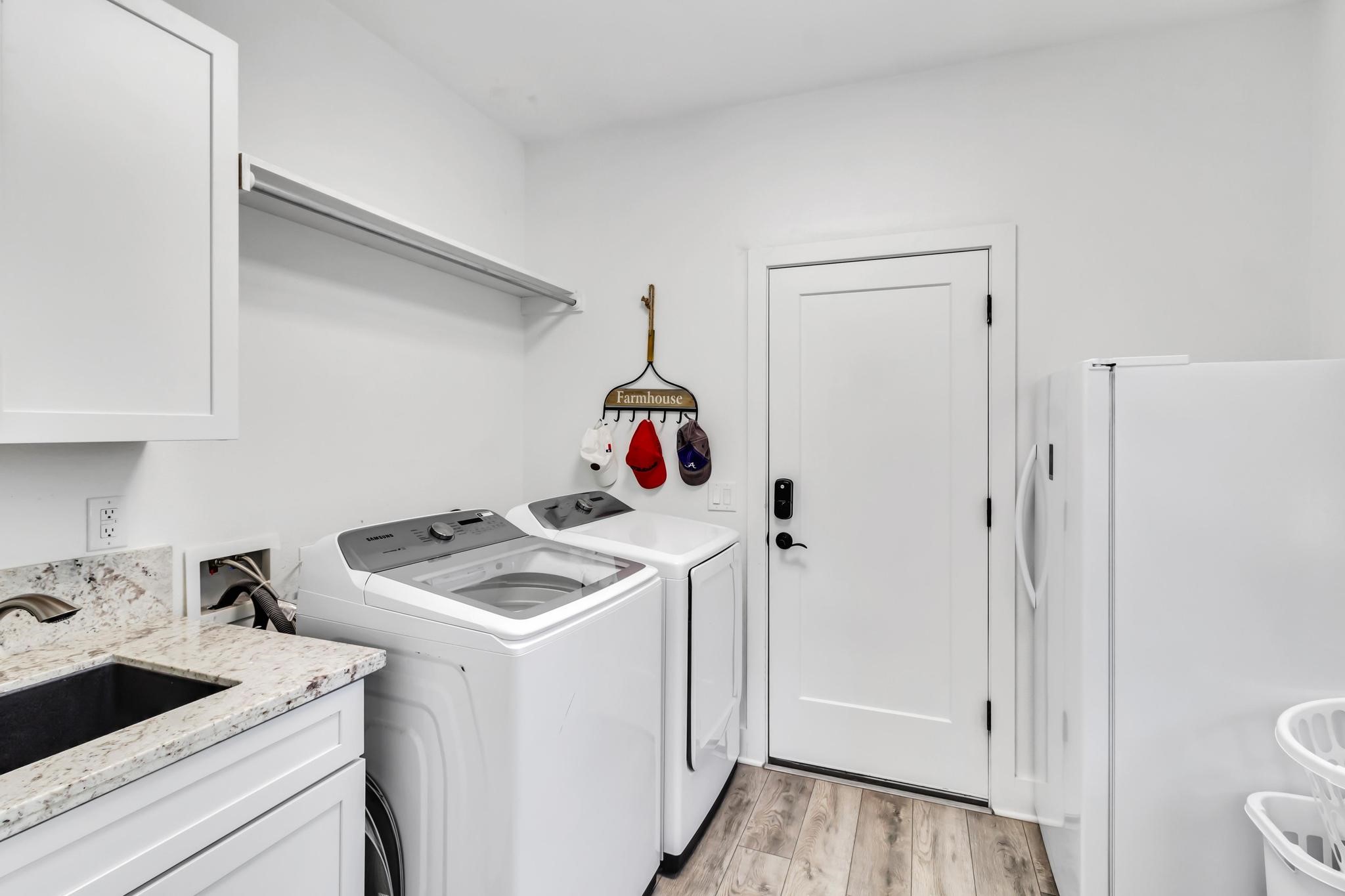 295 County Road 687 Angleton, TX 77515 - Photo 36 of 38 This photo features a modern spacious laundry room with a sleek washer and dryer, a granite countertop with a sink, and ample storage space. The door leads to the oversized, attached garage. There is plenty of room for an additional refrigerator or freezer.
