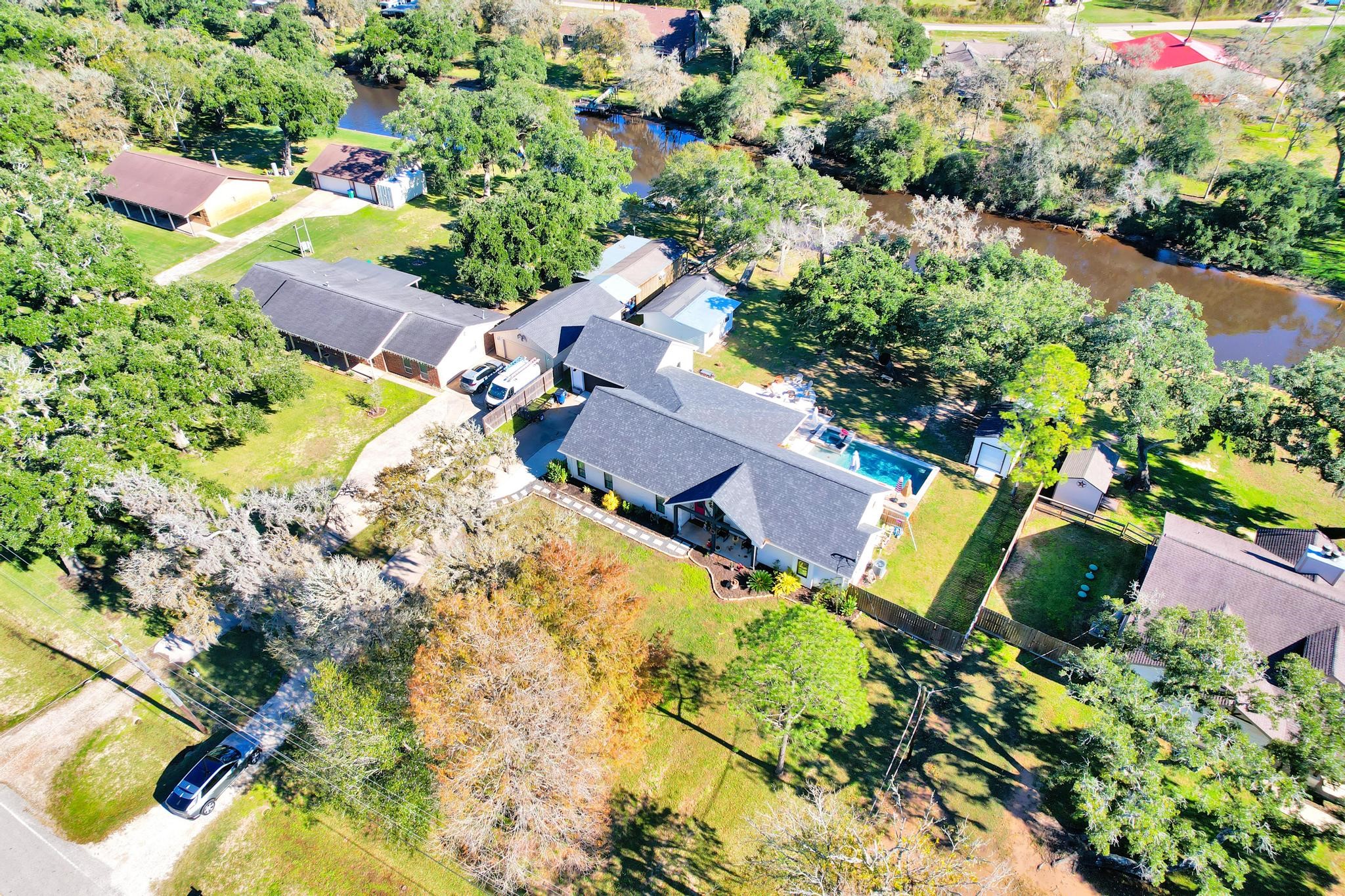 295 County Road 687 Angleton, TX 77515 - Photo 5 of 38 This aerial view showcases a spacious property with a beautiful home, lush greenery, and a pool. It offers a serene riverside setting, with ample outdoor space and neighboring homes in a quiet residential area.