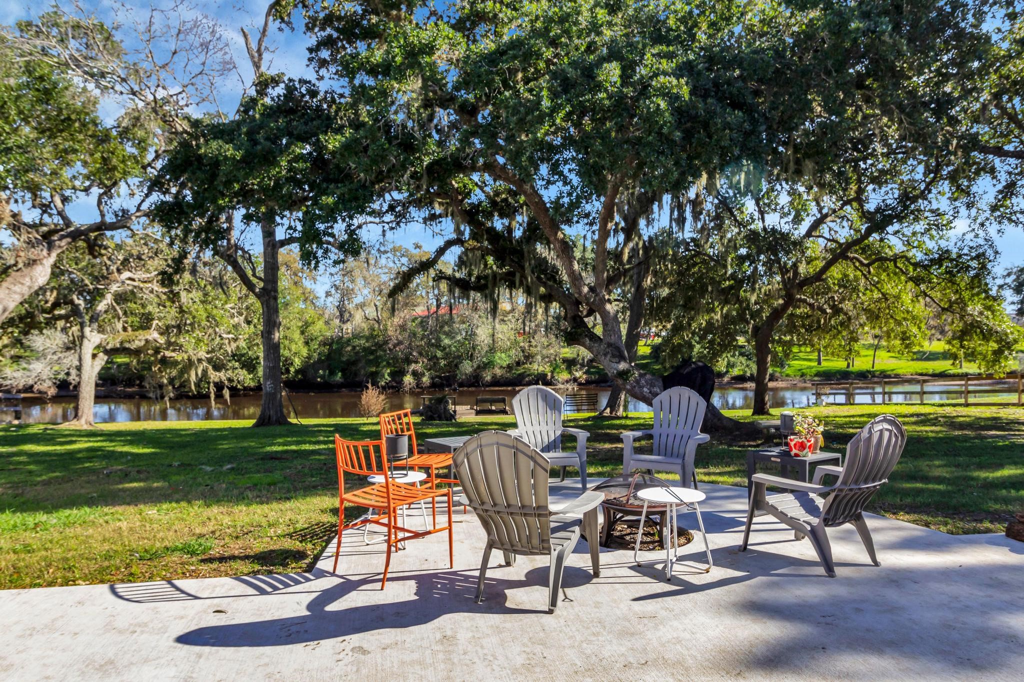 295 County Road 687 Angleton, TX 77515 - Photo 6 of 38 This serene backyard with a concrete patio features comfortable seating around a fire pit. The area is shaded by large trees and overlooks a tranquil waterway, providing a peaceful outdoor retreat.