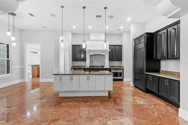 a living room with stainless steel appliances kitchen island granite countertop a refrigerator a sink a stove and white cabinets with wooden floor