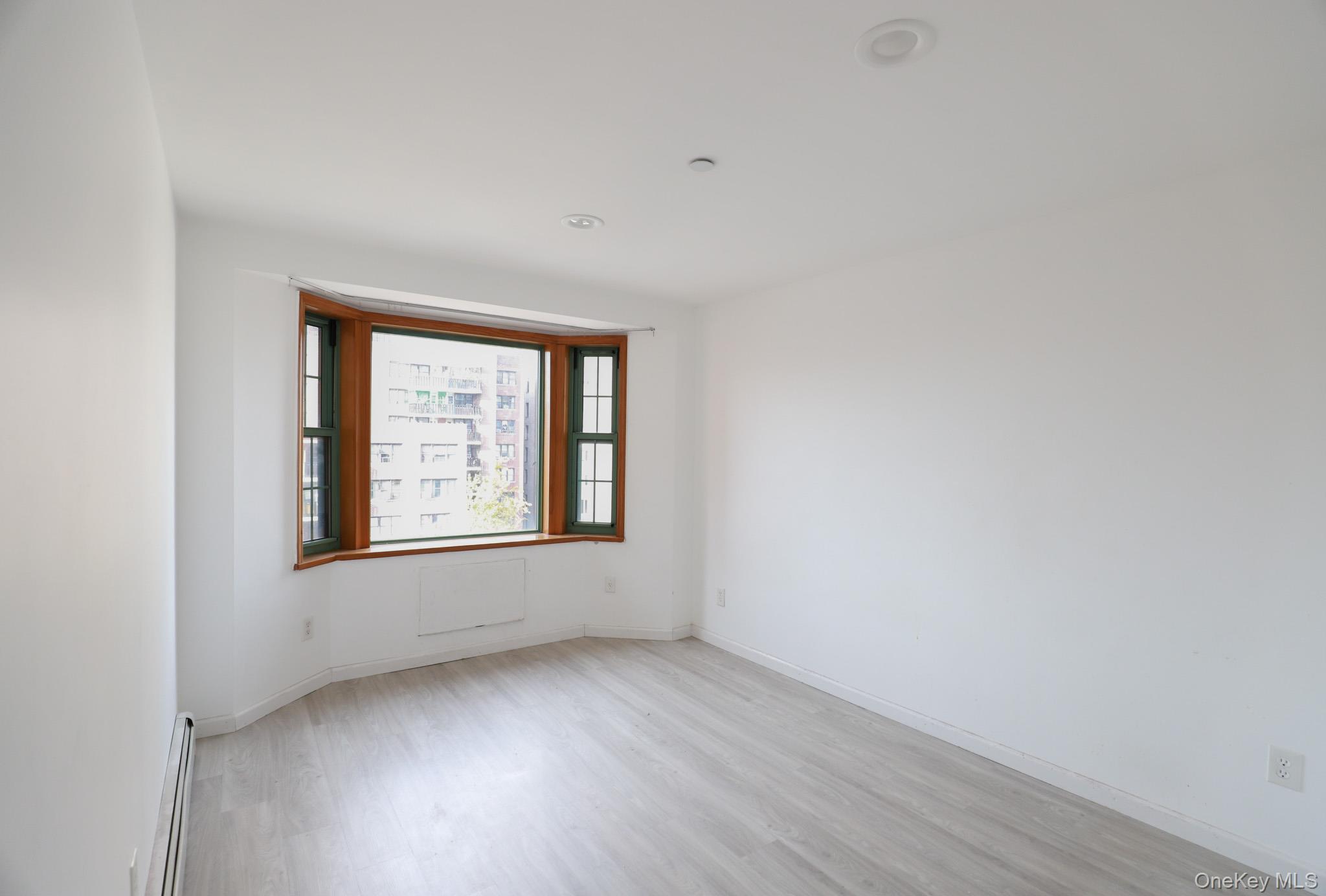 134-43 Maple Avenue, Unit 5B Queens, NY 11355 - Photo 6 of 13 an empty room with wooden floor and windows
