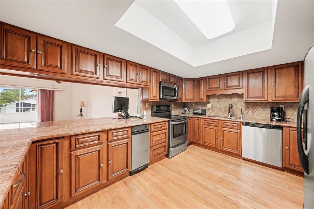 6225 Bayside Drive New Port Richey, FL 34652 - Photo 7 of 31 a kitchen with stainless steel appliances granite countertop a stove top oven a sink dishwasher a dining table and chairs with wooden floor