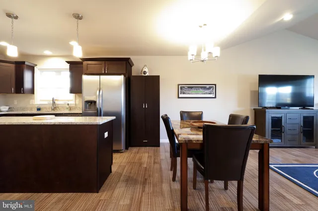 a kitchen with stainless steel appliances granite countertop a refrigerator a stove a sink dishwasher and a dining table with wooden floor