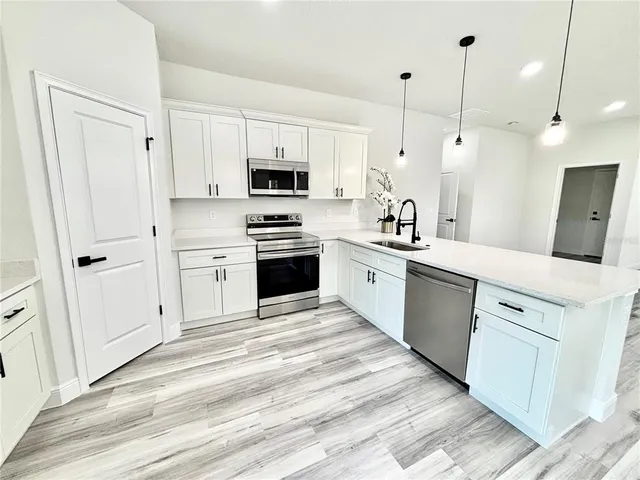 a large white kitchen with stainless steel appliances granite countertop a stove a sink dishwasher and a refrigerator with wooden floor