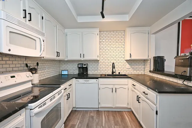 a kitchen with a sink dishwasher a stove and white cabinets with wooden floor