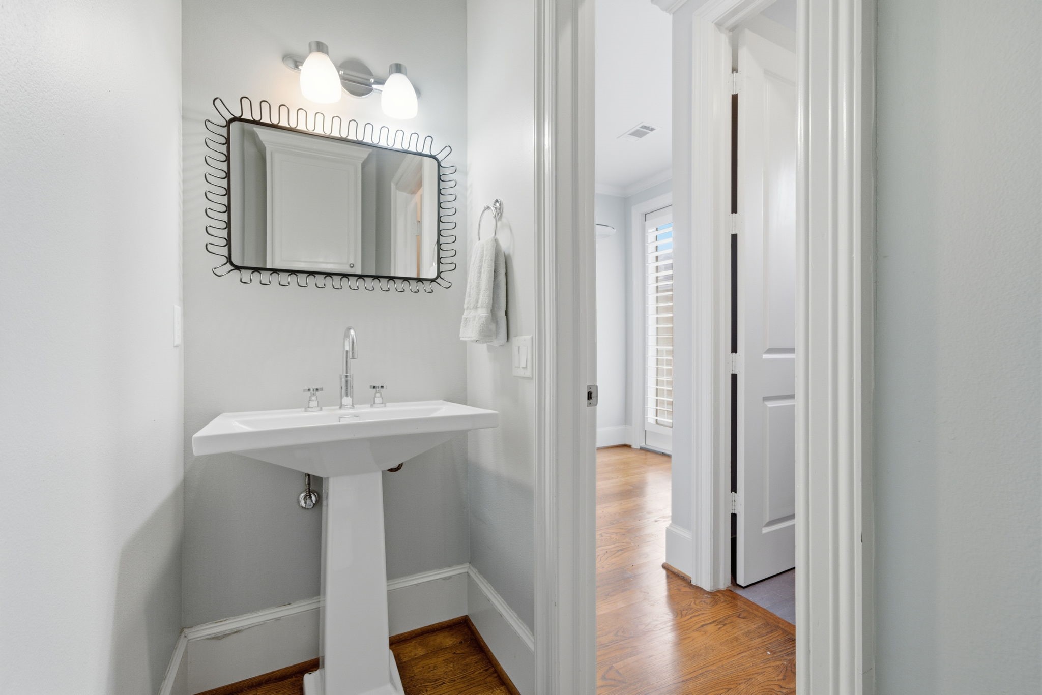 4915 Chenevert Street Houston, TX 77004 - Photo 19 of 41 Modern half bath showcases a sleek pedestal sink, contemporary fixtures, and an eye-catching designer mirror. Conveniently located for guests, the space blends crisp lines and playful updates with a light, airy feel that complements the home’s contemporary style.