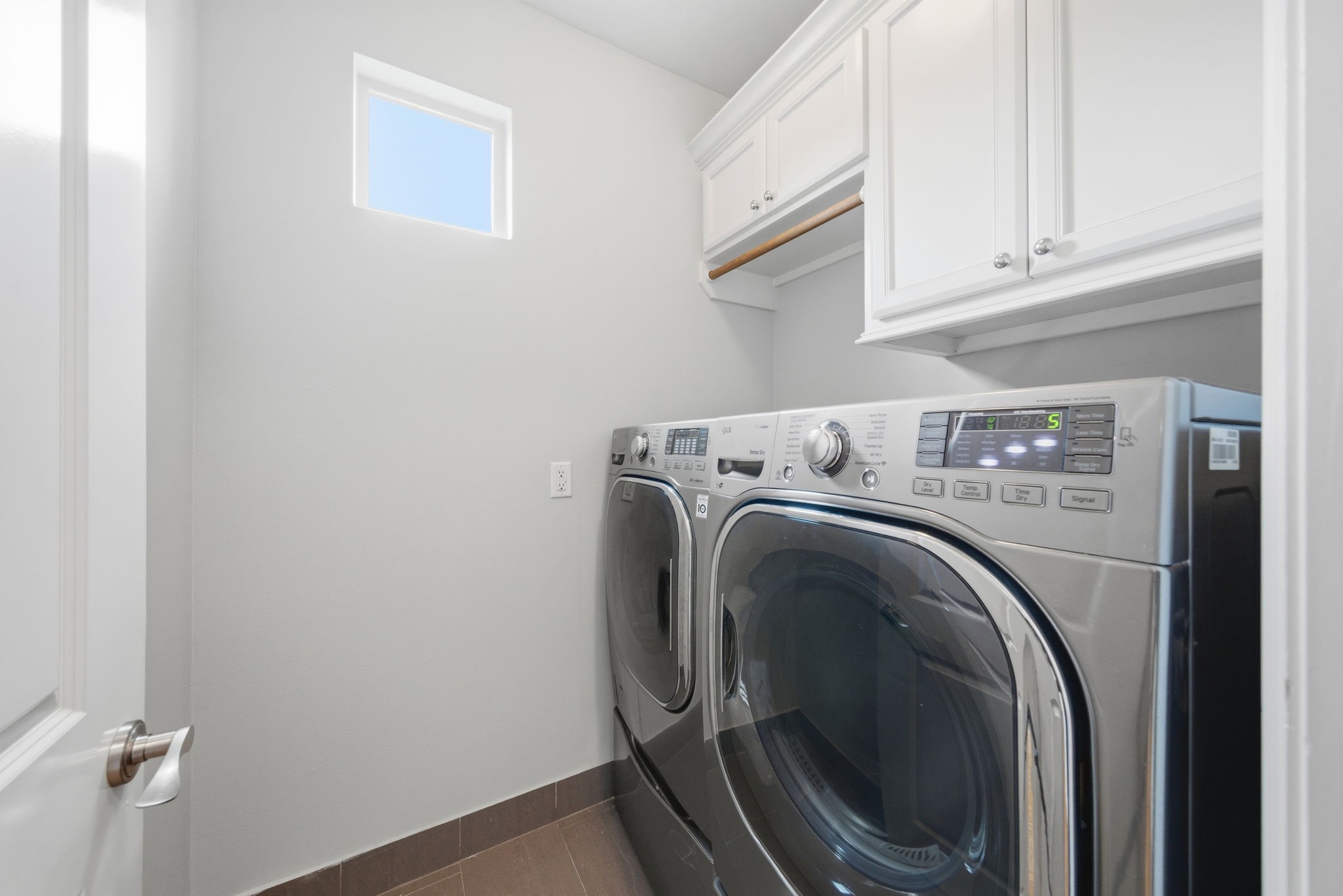 4915 Chenevert Street Houston, TX 77004 - Photo 20 of 41 Dedicated laundry room features side-by-side front-loading washer and dryer, upper cabinetry for organized storage, and a built-in rod for hanging garments. A bright window and neutral tones offer a crisp, contemporary touch, making laundry day effortless in this elevator-capable home.