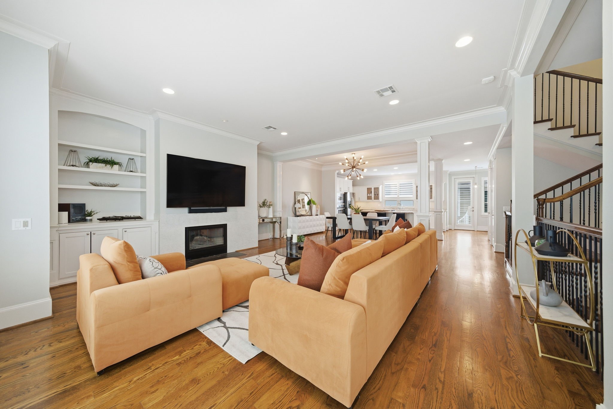 4915 Chenevert Street Houston, TX 77004 - Photo 10 of 41 Open-concept living and dining space offers seamless entertaining with hardwood floors, a contemporary fireplace, and built-in shelving for both style and function. The living area flows effortlessly to the dining area and kitchen, while crown molding and architectural columns elevate the clean, modern aesthetic.