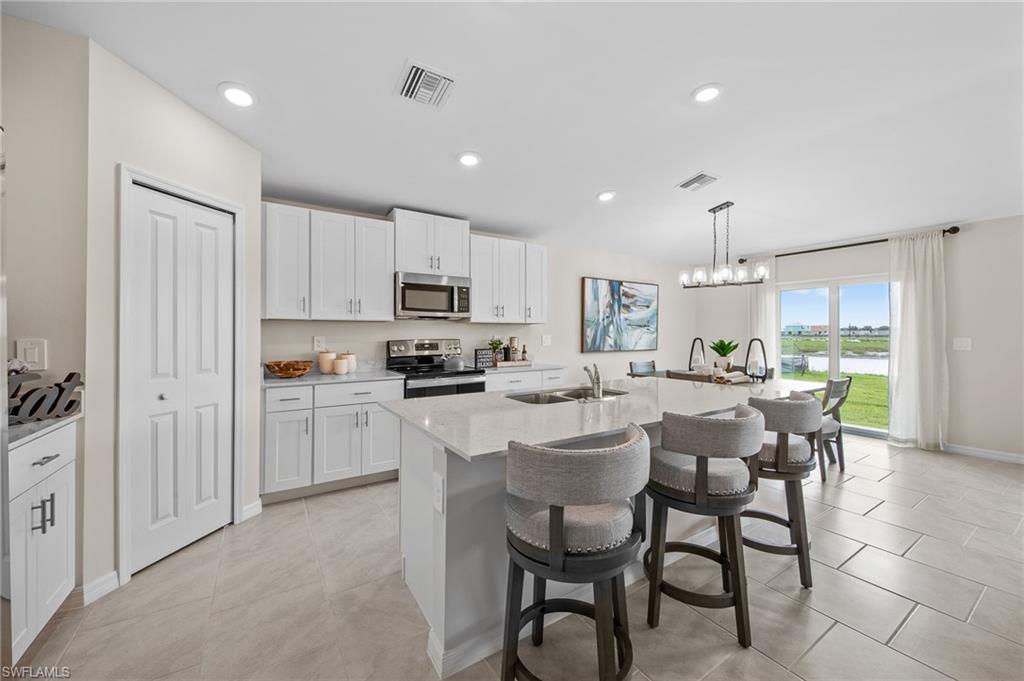 12265 Savanna Lakes Boulevard Lehigh Acres, FL 33936 - Photo 3 of 31 Kitchen featuring appliances with stainless steel finishes, a breakfast bar, a kitchen island with sink, white cabinets, and pendant lighting