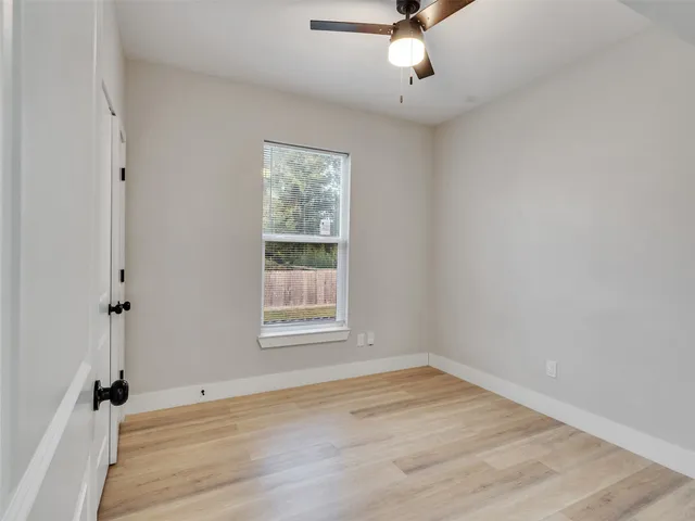 an empty room with wooden floor chandelier fan and windows