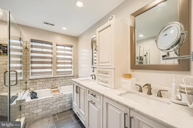 a bathroom with a granite countertop double vanity sink large mirror and a bathtub