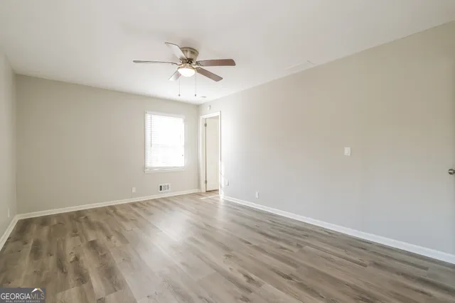an empty room with wooden floor fan and windows