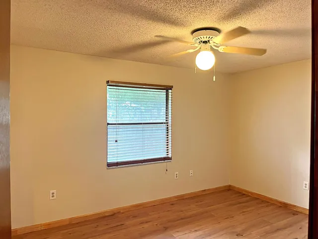 an empty room with wooden floor fan and windows