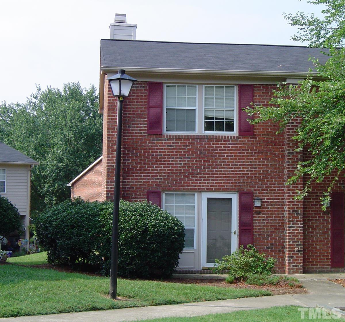 a brick house with a small yard plants and large tree