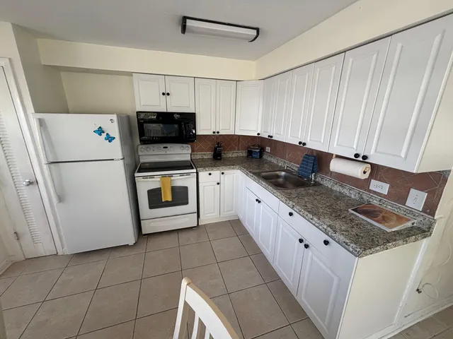 a kitchen with granite countertop a sink a stove top oven a refrigerator and cabinets