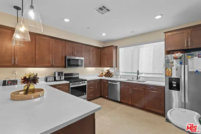 a kitchen with stainless steel appliances granite countertop a sink dishwasher stove top oven and refrigerator with wooden cabinets