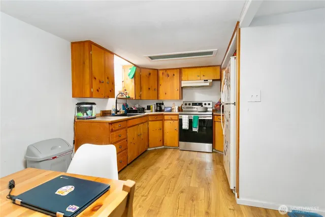 a kitchen with stainless steel appliances a refrigerator a sink a stove top oven and a dining table with wooden floor