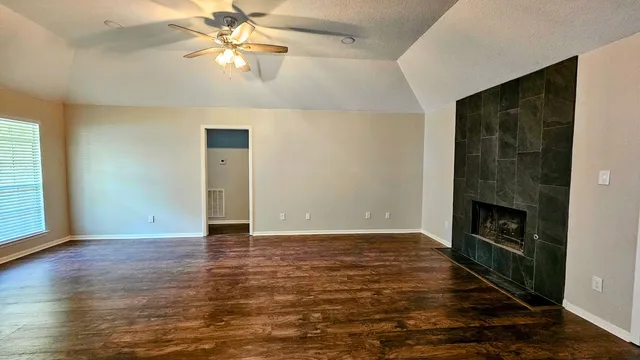 an empty room with wooden floor a ceiling fan and windows