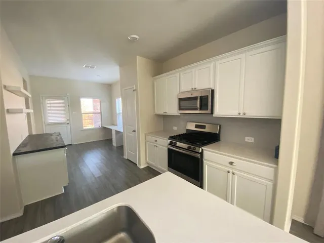 a kitchen with stainless steel appliances granite countertop a refrigerator a stove top oven a sink dishwasher and white cabinets with wooden floor