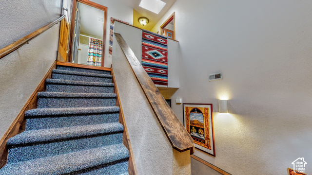 3299 Fairway Loop Moab, UT 84532 - Photo 7 of 23 Staircase featuring wood-finish handrails and blue carpeting, with white wall sconces providing illumination