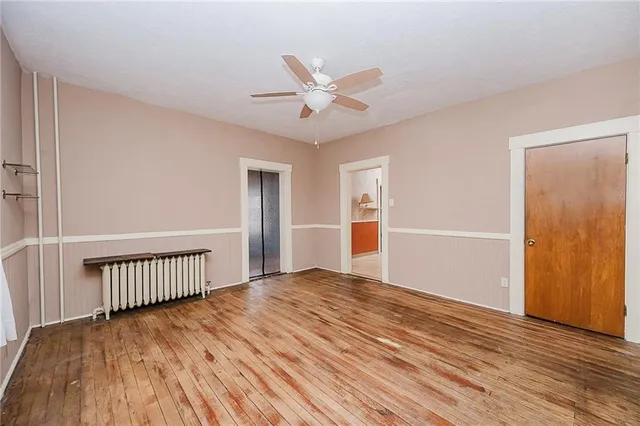 a view of an empty room with wooden floor and a ceiling fan