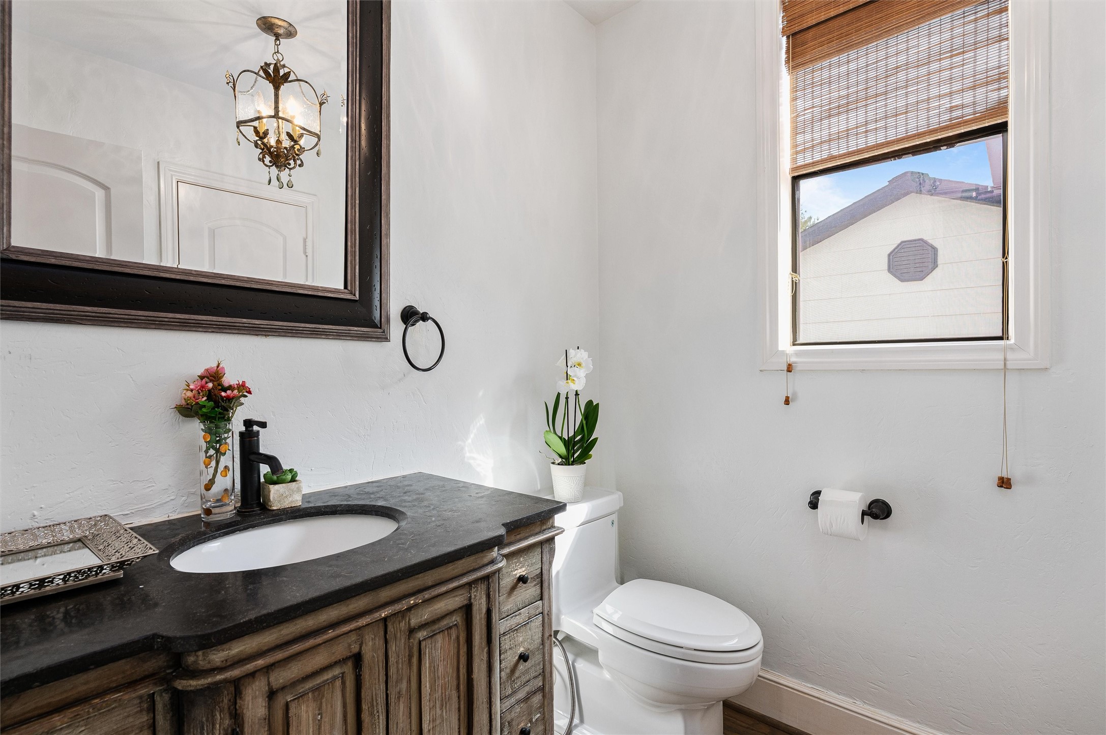 4523 Maple Street Bellaire, TX 77401 - Photo 22 of 50 The powder bathroom on the first floor boasts an updated vanity with bronze finishes, a framed mirror, and an elegant lighting fixture. A window allows natural light to brighten the space.