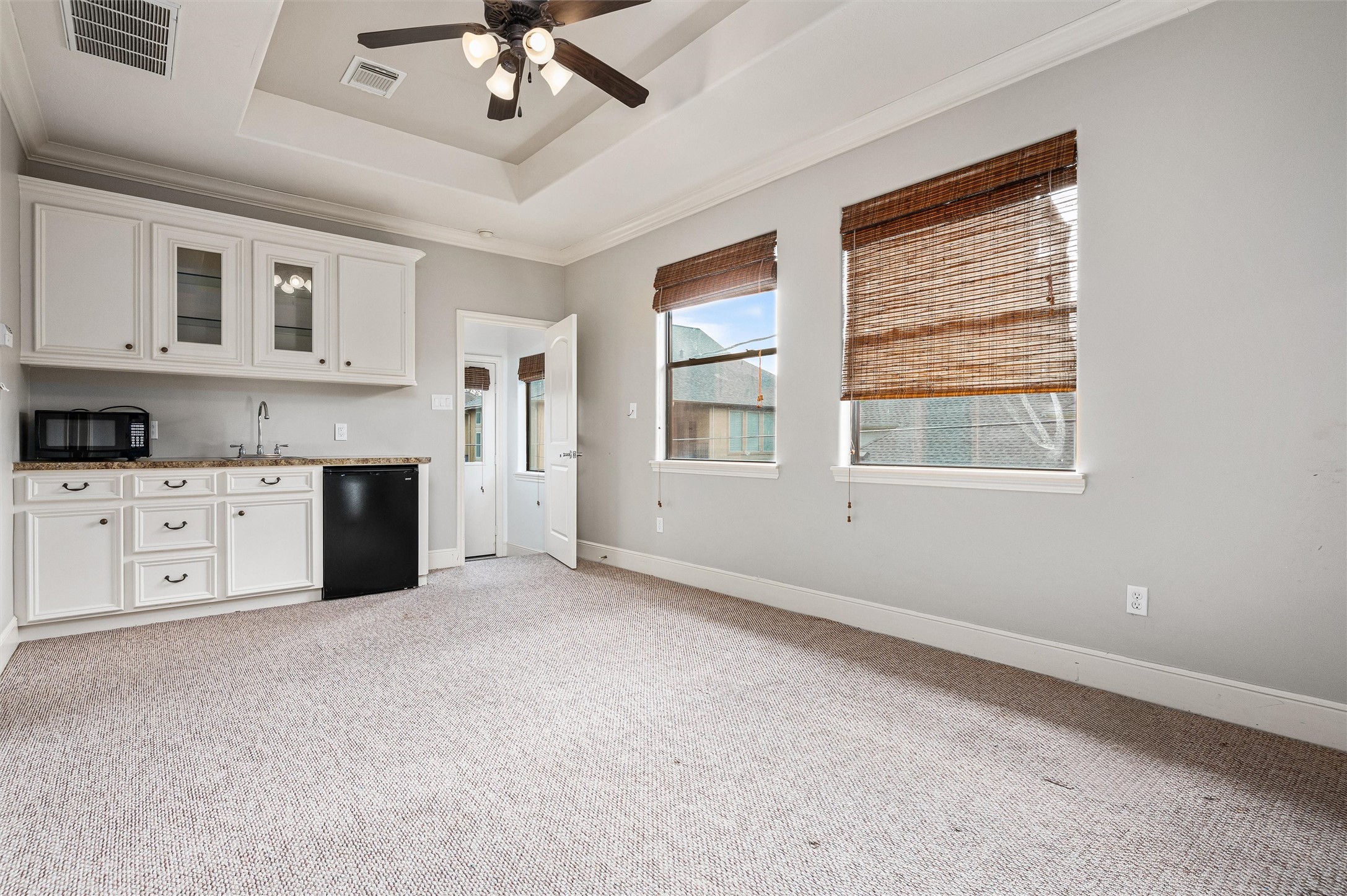 4523 Maple Street Bellaire, TX 77401 - Photo 33 of 50 Welcome to the garage apartment or bonus room, featuring plush carpet, a tray ceiling with a ceiling fan, and two large windows that fill the space with natural light. The space includes a wet bar with a sink and refrigerator, complemented by upper and lower cabinets for convenient storage of essentials.