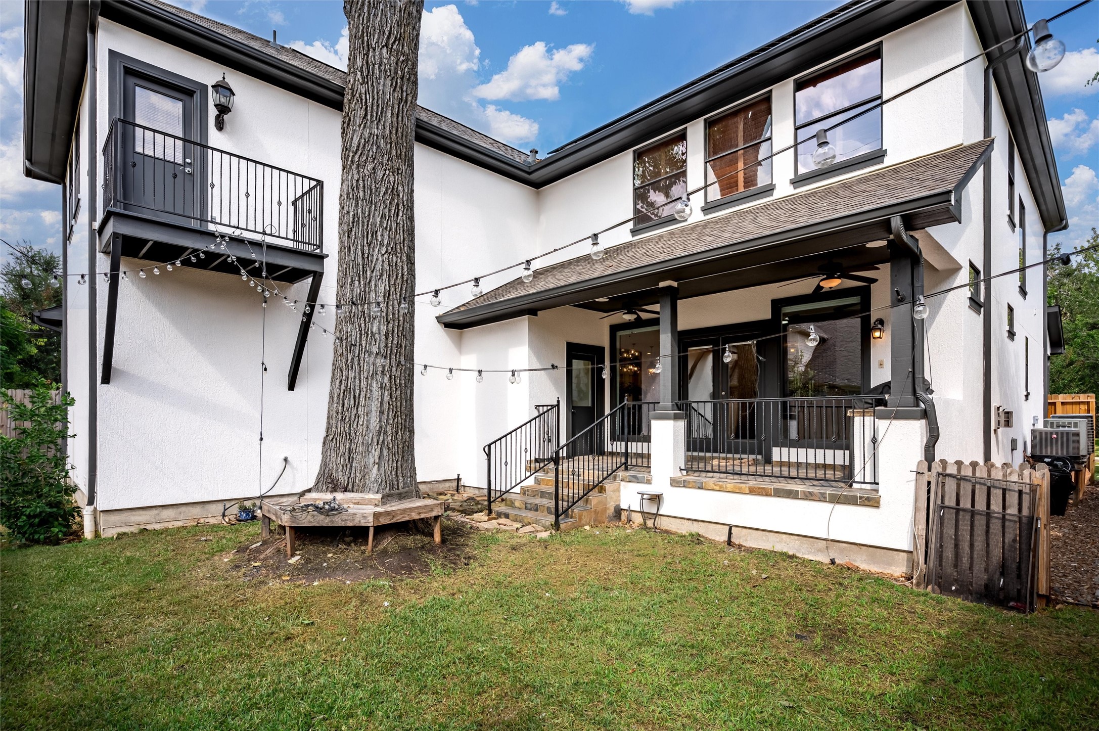 4523 Maple Street Bellaire, TX 77401 - Photo 45 of 50 Stairs from the covered porch lead down to a lush green space, perfect for pets to roam or for family play. A custom wooden bench wraps around a towering tree, adding charm and functionality to the yard.
