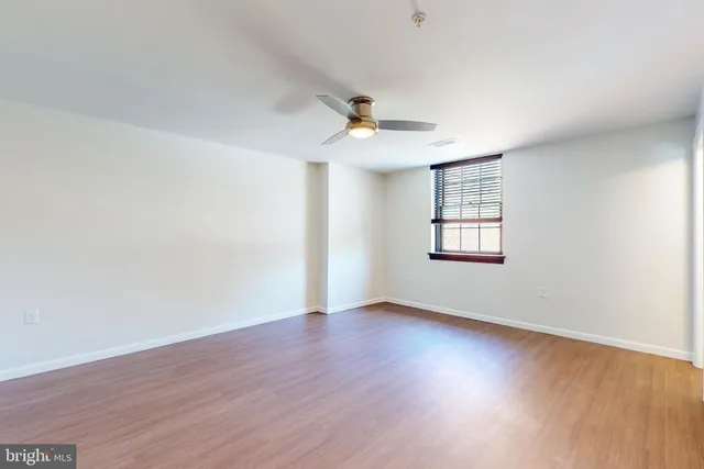 an empty room with wooden floor ceiling fan and windows