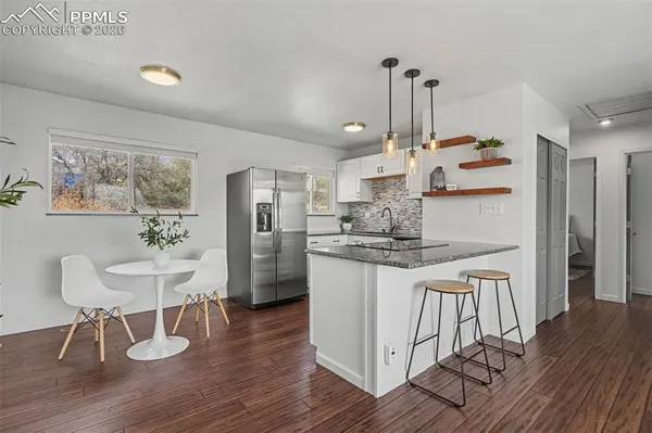 a kitchen with stainless steel appliances granite countertop a refrigerator a stove a sink dishwasher and a dining table with wooden floor
