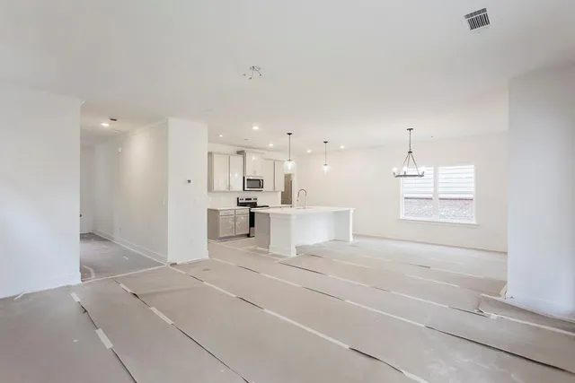 a view of an empty room with kitchen and window
