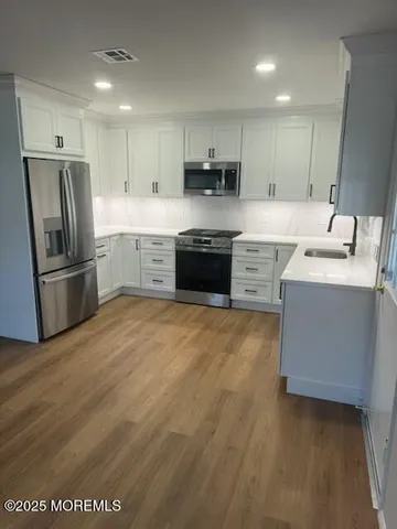 a large kitchen with stainless steel appliances granite countertop a stove a sink dishwasher a refrigerator and a oven with wooden floors