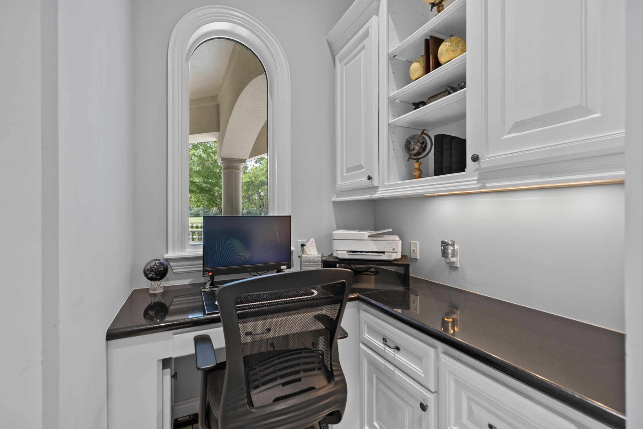 39 Maymont Way Spring, TX 77382 - Photo 15 of 50 This photo shows a compact home office space with a sleek, black countertop and built-in white cabinetry. A window provides natural light, and there's a desk setup with a chair, computer, and printer. The area is well-organized, making it ideal for productivity.