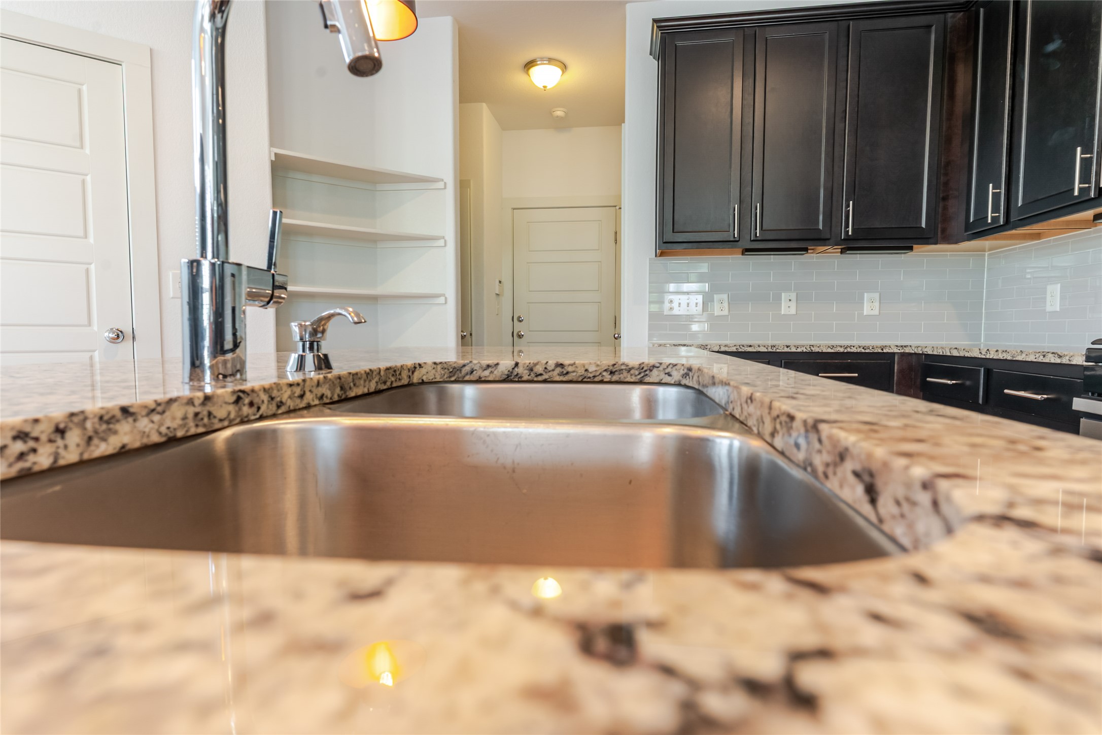 1400 Homespun Road Austin, TX 78745 - Photo 11 of 30 Granite countertops and dark cabinetry flank a double basin stainless steel kitchen sink.