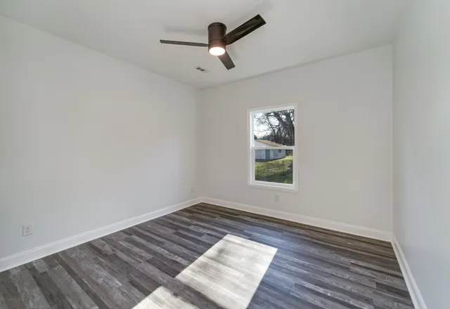 an empty room with wooden floor ceiling fan and window