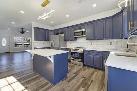 a kitchen with kitchen island granite countertop a sink dishwasher stove and cabinets with wooden floor