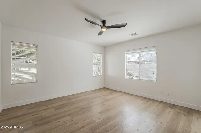 an empty room with wooden floor fan and windows