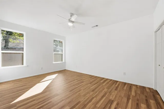 an empty room with wooden floor closet and windows