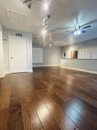 an empty room with wooden floor kitchen view and windows