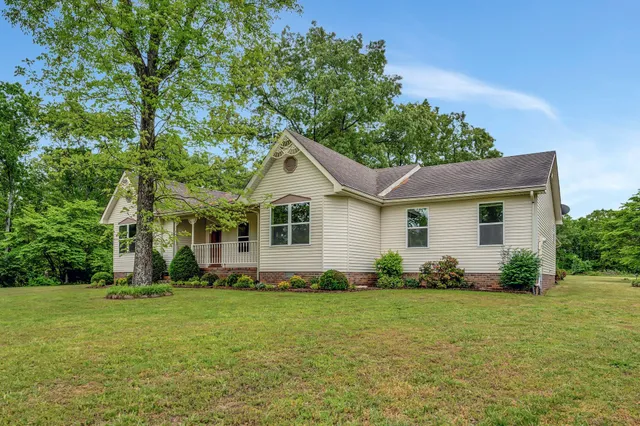 a view of a yard in front of a house with plants and large tree