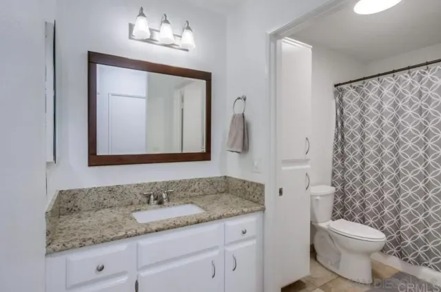 a bathroom with a granite countertop sink vanity mirror and toilet