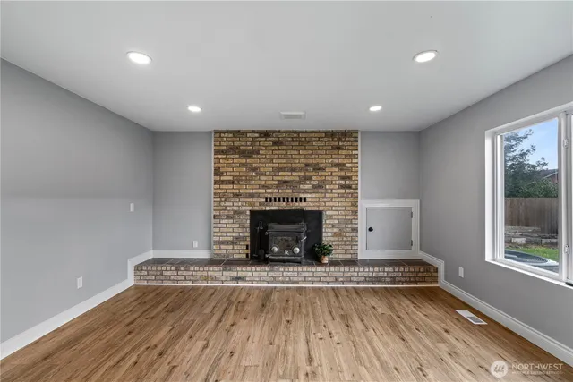 an empty room with wooden floor a fireplace and windows